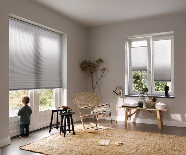 Woonkamer met houten meubelen, lichtgrijze tegelvloer, accessoires van keramiek en elektrische raamdecoratie op maat.