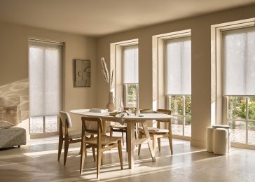 Woonkamer in natuurlijke beige- en wittinten met ovale tafel, houten stoelen en Duettes als elektrische raamdecoratie.