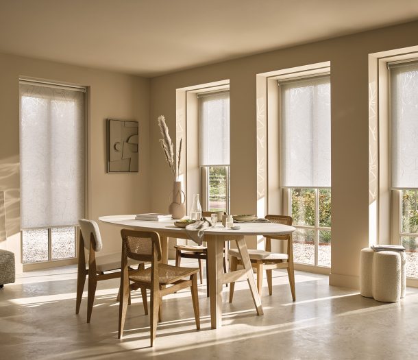 Woonkamer in natuurlijke beige- en wittinten met ovale tafel, houten stoelen en Duettes als elektrische raamdecoratie.