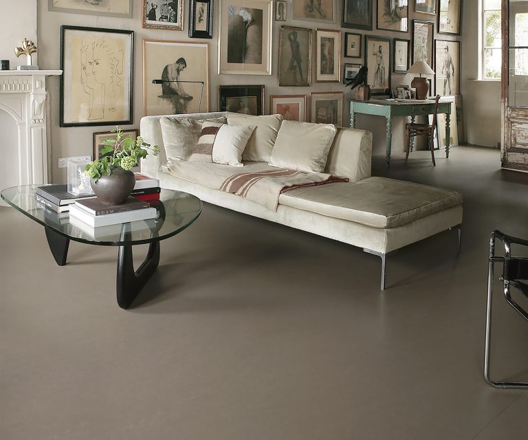 Moderne woonkamer met donkergrijze marmoleum vloer, glazen salontafel, beige bank en kunst aan de muur