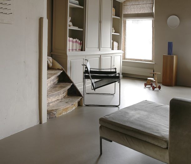 Woonkamer met witte houten kast, beige vouwgordijnen, fluwelen bank en grijze marmoleum vloer