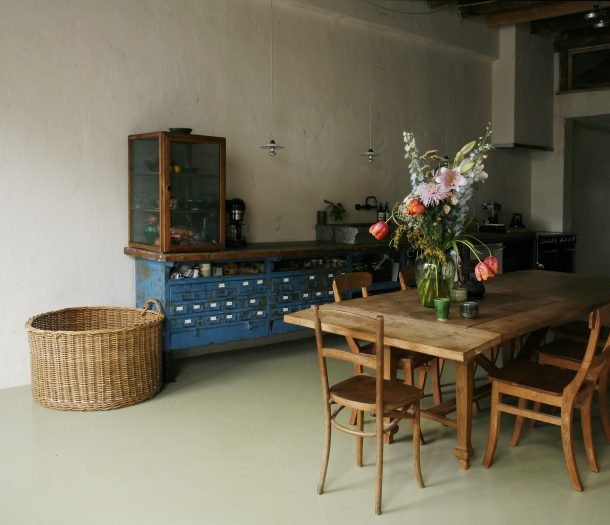 Keuken in robuuste stijl met houten tafel, fornuis, werkbank als aanrecht en lichtgroene marmoleum vloer