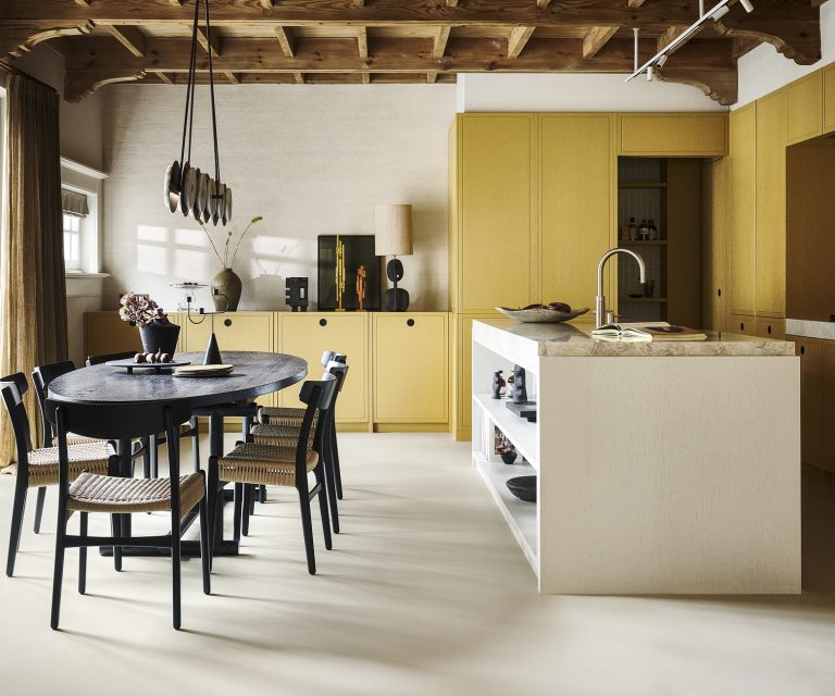 Keuken met houten kasten, kookeiland, houten tafel met rieten stoelen en een lichtgrijze marmoleum vloer