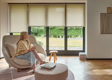Beige/licht gele rolgordijnen in de woonkamer met een dame op een stoel