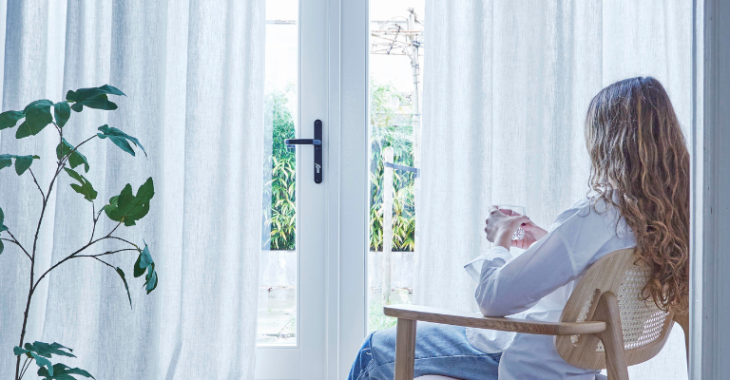 Een dame voor openslaande deuren met witte inbetweengordijnen
