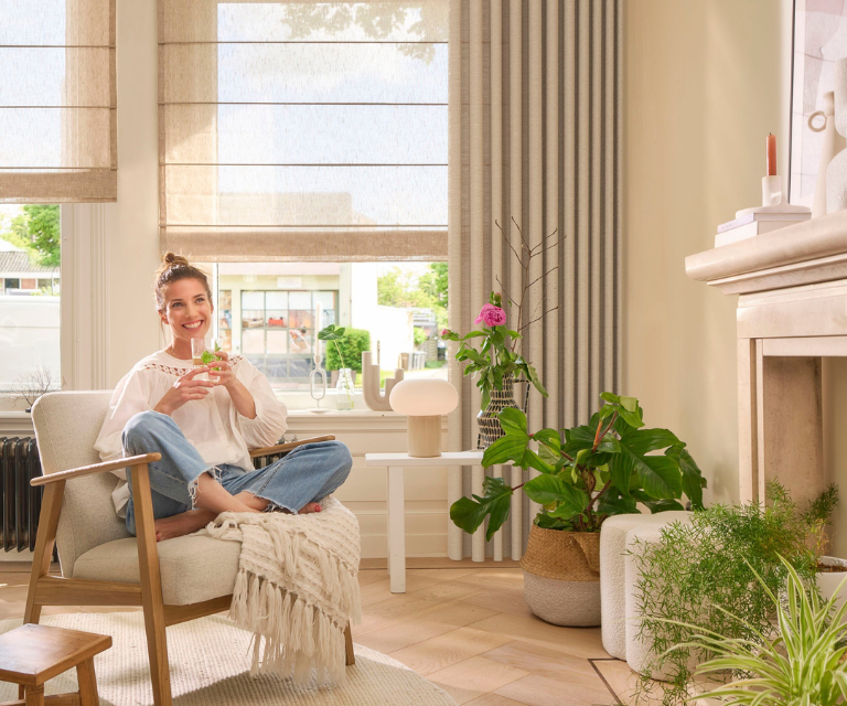 Vrouw in stoel in woonkamer met beige vouwgordijnen en gordijnen