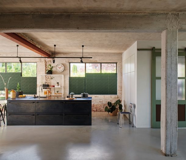 Industriele woonstijl keuken in grote hal met zwart keukenblok en groene plisségordijnen