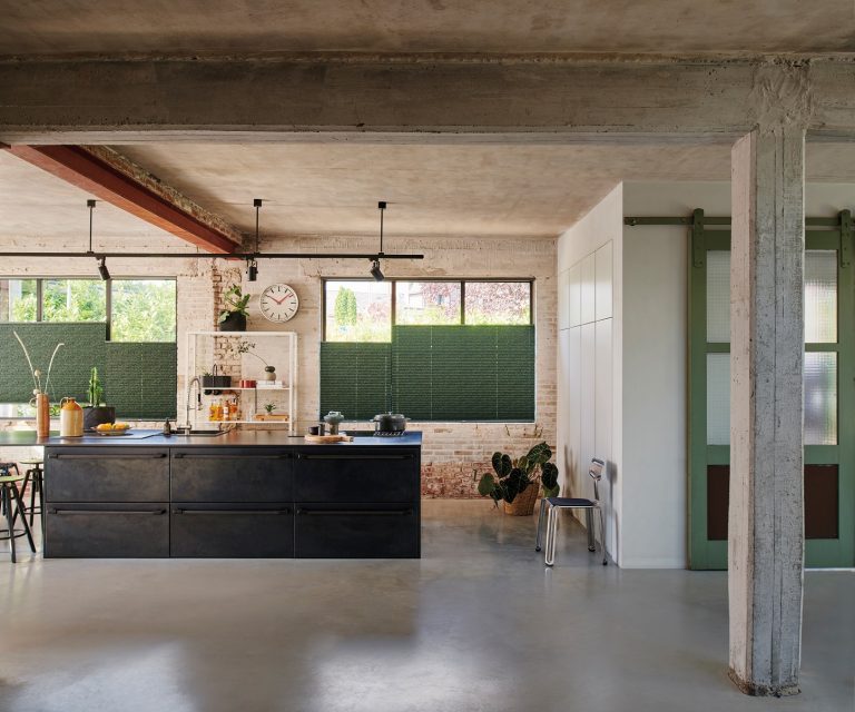 Industriele woonstijl keuken in grote hal met zwart keukenblok en groene plisségordijnen