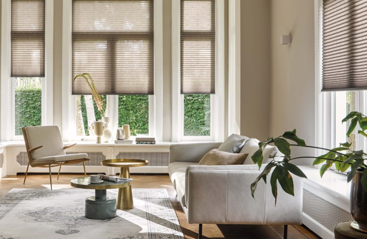 Woonkamer in hotel chique stijl met bank, leesstoel, vloerkleed en beige plissé shades.