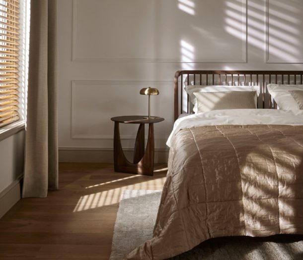 Slaapkamer in hotel chique stijl met luxe bed, houten vloer, vloerkleed , beige overgordijnen en horizontale jaloezieën