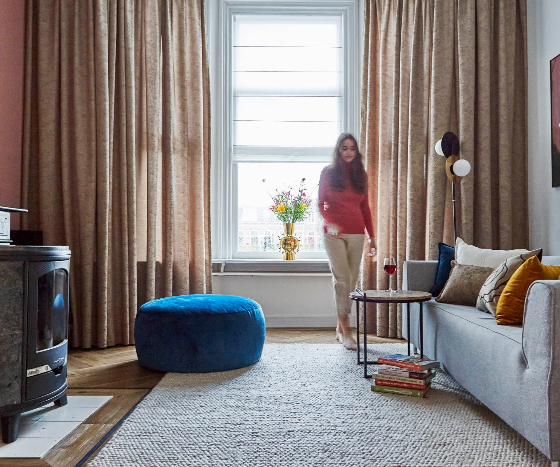 Licht bruine overgordijnen in woonkamer met vrouw, grijs vloerkleed en grijze bank Licht bruine overgordijnen in woonkamer met vrouw, grijs vloerkleed en grijze bank