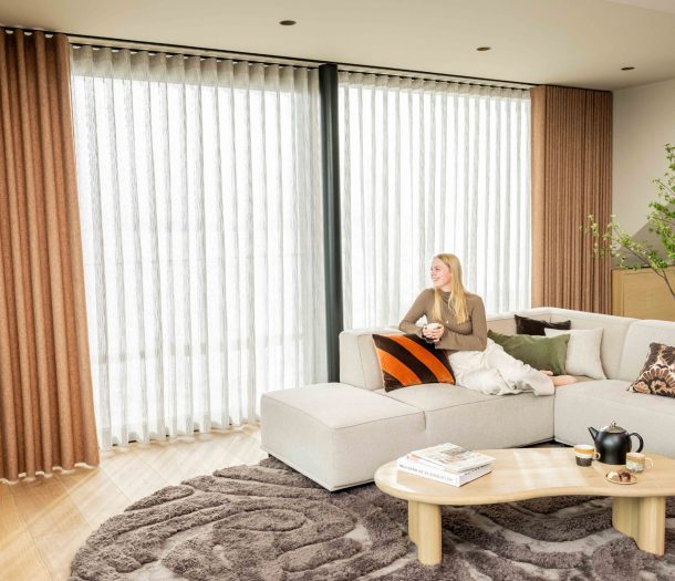 Lichte inbetweens en bruine overgordijnen in de woonkamer met grijze hoekbank en vloerkleed Lichte inbetweens en bruine overgordijnen in de woonkamer met grijze hoekbank en vloerkleed