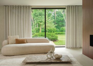 Grijze overgordijnen in de woonkamer met beige bank en licht vloerkleed