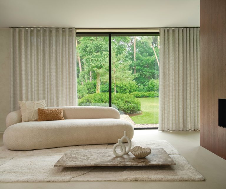 Grijze overgordijnen in de woonkamer met beige bank en licht vloerkleed