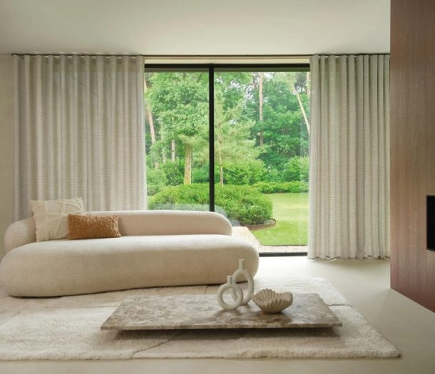 Grijze overgordijnen in de woonkamer met beige bank en licht vloerkleed