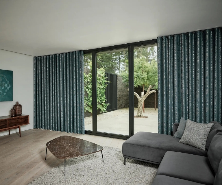 Blauwe/zilvere overgordijnen in woonkamer met grijze hoekbank en fluffy grijs vloerkleed
