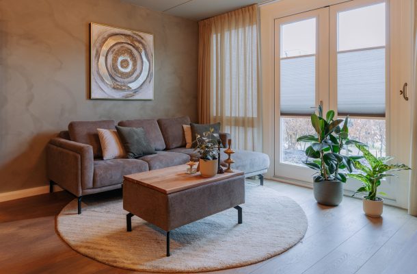 Woonkamer met 3zitsbank, rond vloerkleed en houtlook pvc vloer brede planken