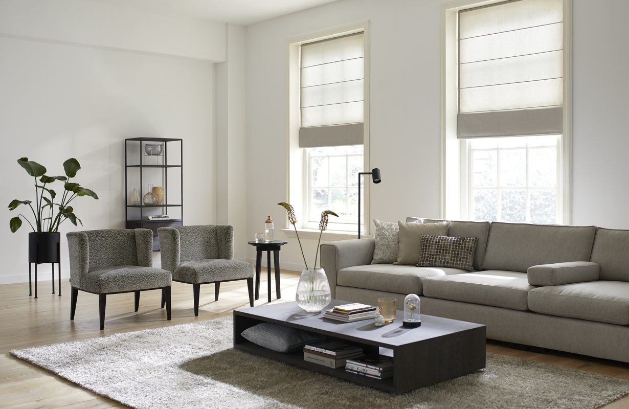 Woonkamer met bank in beige, rechthoekig vloerkleed en vouwgordijnen