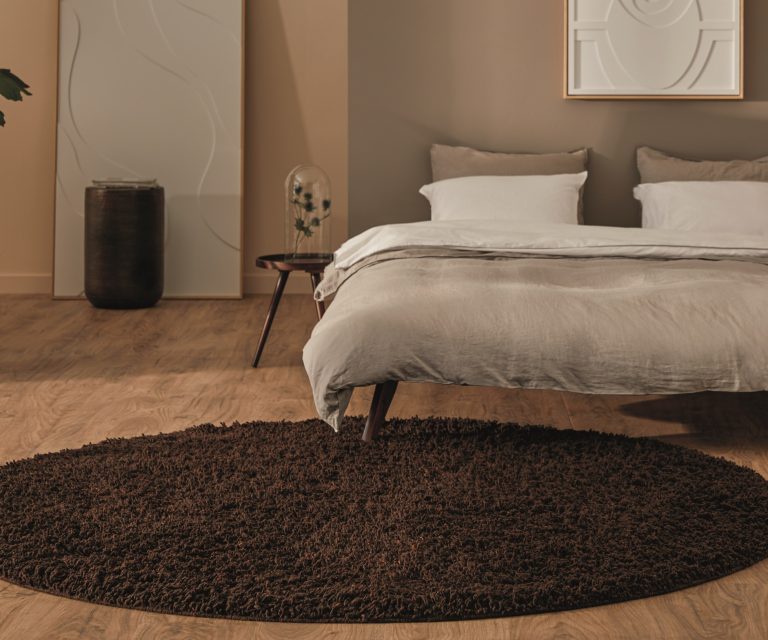 Slaapkamer met tweepersoons bed en rond zacht vloerkleed in warme bruintint