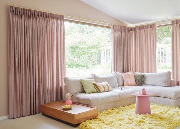 Roze gordijnen, geel hoogpolig vloerkleed in woonkamer met grijze hoekbank