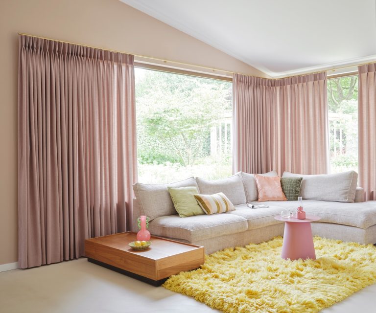 Roze gordijnen, geel hoogpolig vloerkleed in woonkamer met grijze hoekbank
