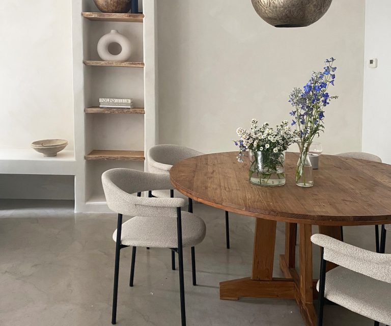 Eetkamer met ronde houten tafel en boucle stoelen tegen een muur in warm wit stucwerk van Pure & Original, met een nis vol decoratie.