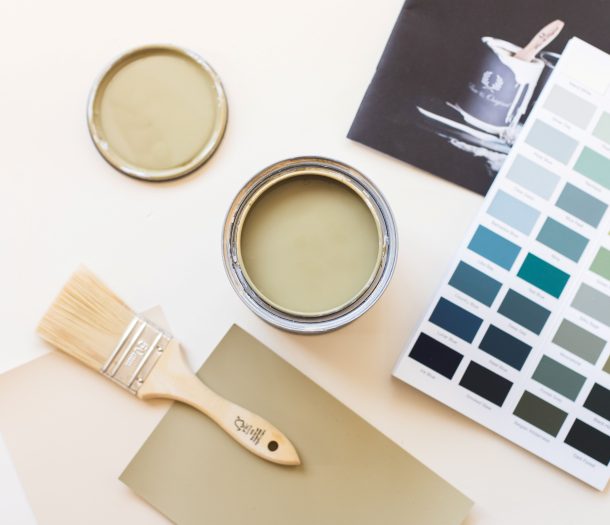 Flatlay met een open verfblik in olijfgroen, een kwast en kleurenkaarten van Pure & Original.