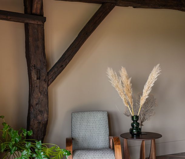 Eetkamer met ronde houten tafel en boucle stoelen tegen een muur in warm wit stucwerk van Pure & Original, met een nis vol decoratie.