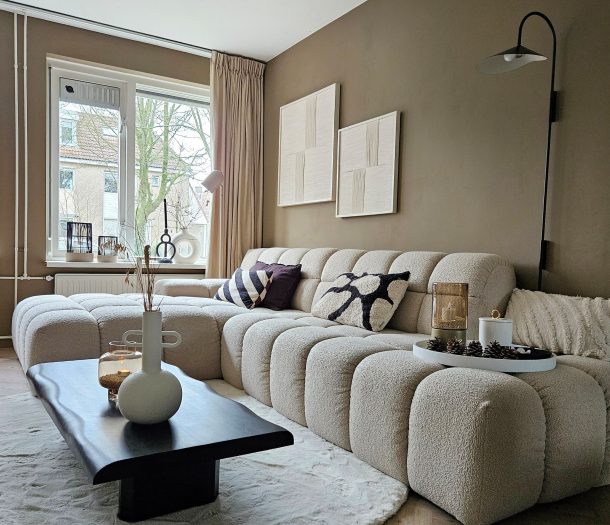 Zithoek met een gestoffeerde fauteuil en houten bijzettafel tegen een muur in kaki stuclook, onder oude houten balken.