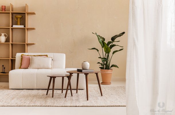 Zithoek met een crème boucle bank tegen een zachtgele muur, met een houten kast en een grote plant.