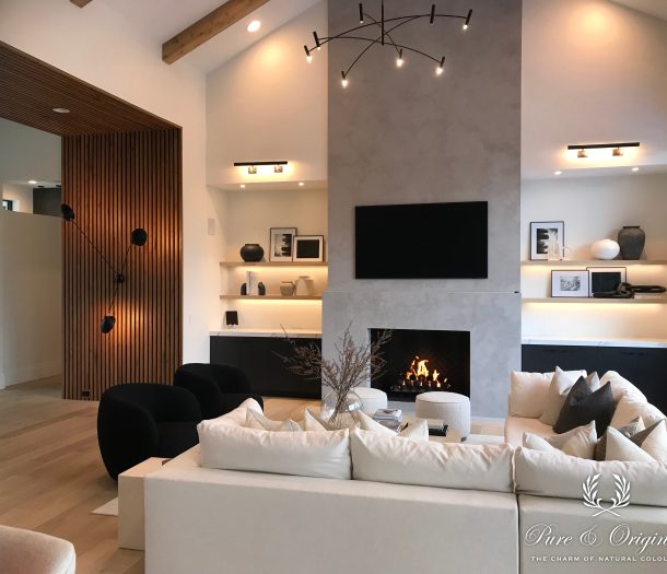 Woonkamer met een hoge stucwand rond de open haard, zwevende wandplanken en een lichte hoekbank.