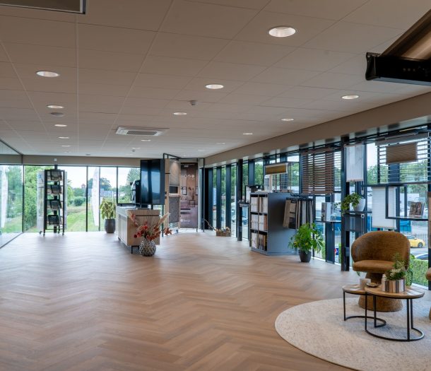 Lichte showroom van Althoff Woonmode met visgraatvloer, raamdecoratie zoals jaloezieën en plissés langs de ramen en een zithoek met fauteuils
