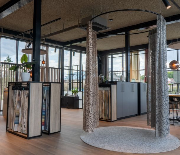 Showroom van Althoff Woonmode met een rond opgehangen vitrage met grafisch patroon, rekken met gordijnstalen en een tafel om stoffen te bekijken