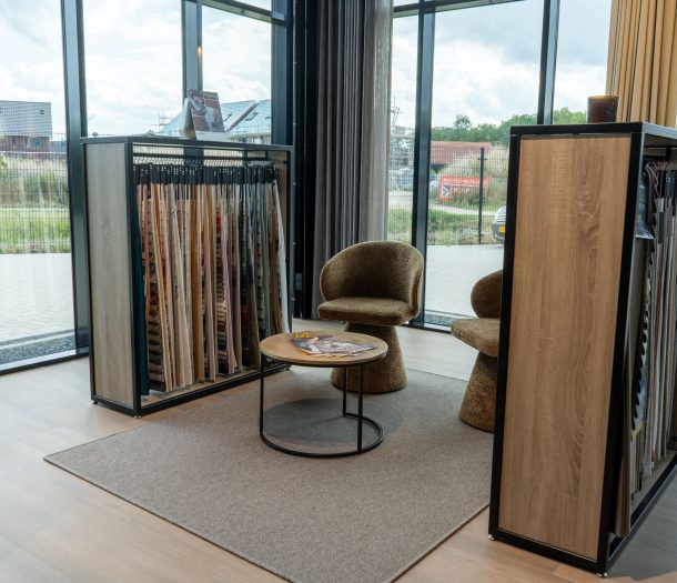 Gezellige zithoek in de showroom van Althoff Woonmode met twee teddy stoelen, een ronde bijzettafel en gordijnstalen op een vloerkleed
