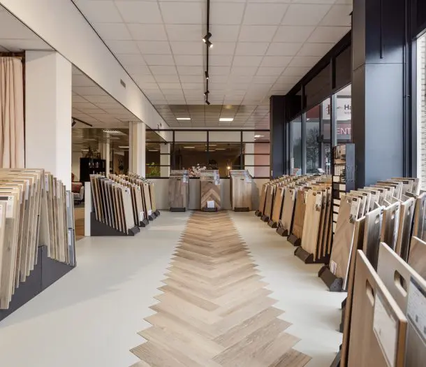 Vloerenafdeling in de showroom in Ede met rekken vol vloerstalen en een visgraatvloer met lichte houtlook in het midden van het pad